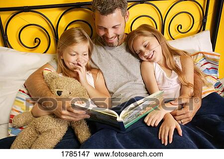 Stock Photo - A father reading to his children in bed.. Fotosearch