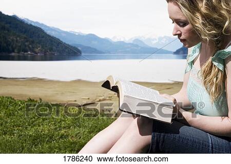 Stock Image - A Woman reading by the lake. Fotosearch