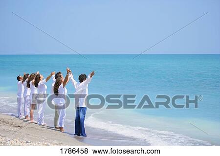 Stock Photo - Group of people with arms raised at the seaside. Fotosearch