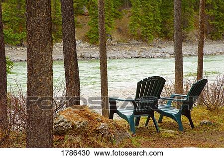 Stock Image - Lawn chairs situated by the lake. Fotosearch