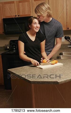 Stock Image - Man kissing woman in kitchen. Fotosearch