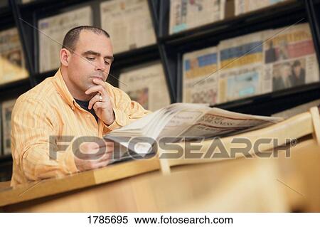 Stock Photography - Man reading newspaper in library. Fotosearch