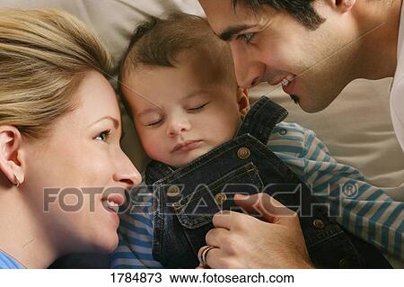Stock Image - Parents waking up baby. Fotosearch