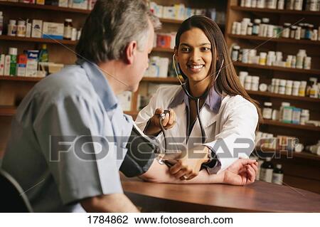 Stock Image - Pharmacist taking patients blood pressure. Fotosearch