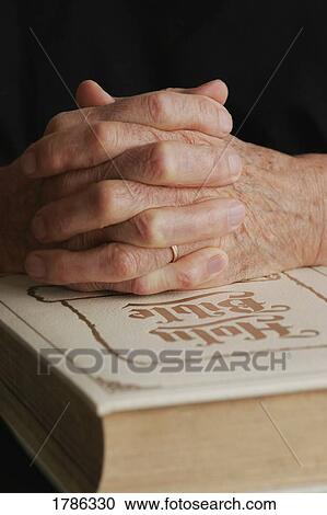 Stock Image - Senior's folded hands on Holy Bible. Fotosearch