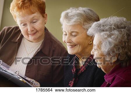 Three ladies looking at a photo album View Large Photo Image Picture - Three ladies looking at a photo album. Fotosearch
