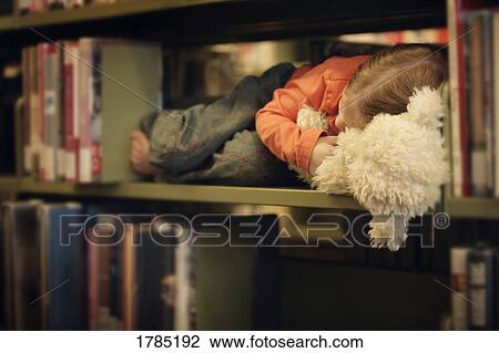 Stock Image - Toddler falls asleep in a book shelf. Fotosearch