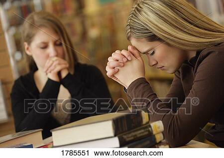 Stock Image - Two women praying in library. Fotosearch