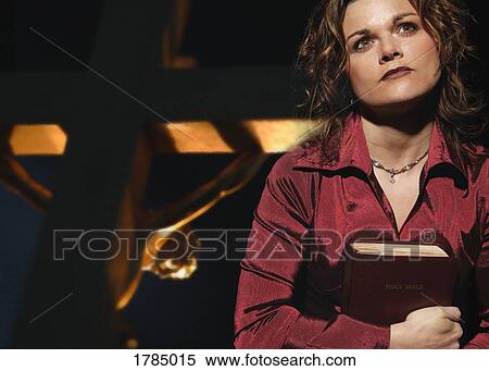 Stock Photography - Woman holding bible with Jesus on cross in background. Fotosearch