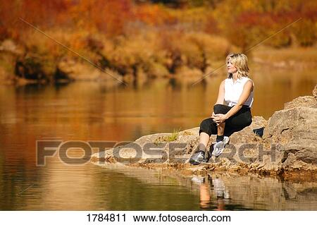 Stock Image - Woman sitting by a scenic pond. Fotosearch