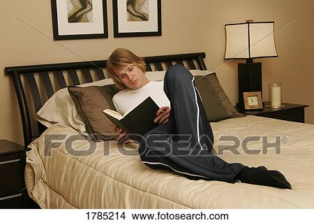 Picture - Young man reading on his bed. Fotosearch