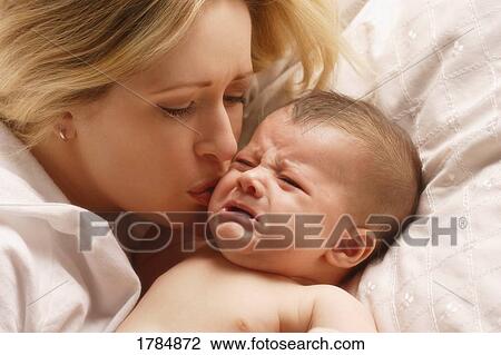 Stock Image - Young mother kissing crying baby. Fotosearch