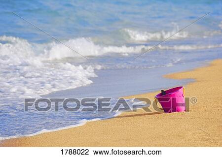 Stock Image - A beach bucket sitting at the waters edge. Fotosearch