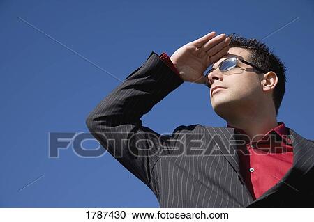 Stock Image - A man shields his eyes from the sun and looks into the distance. Fotosearch