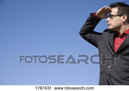 Stock Image - A man shields his eyes from the sun and looks into the distance. Fotosearch