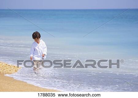 Stock Photography - A young boy walks in water on the shoreline. Fotosearch
