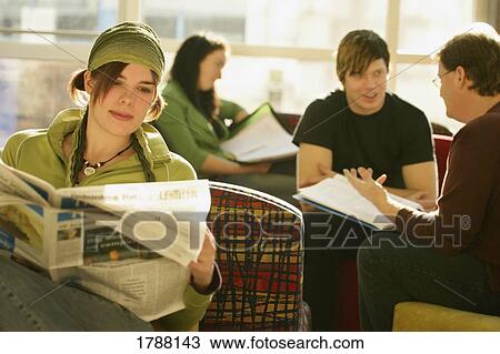Stock Image - A young woman reads the newspaper among other individuals. Fotosearch