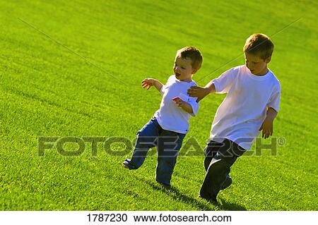 Stock Image - Little boys running across a stretch of grass. Fotosearch