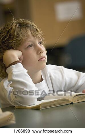 Young boy pondering over book View Large Photo Image Stock Photo - Young boy pondering over book. Fotosearch