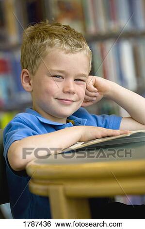 Young boy sitting with books at the library View Large Photo Image Stock Photograph - Young boy sitting with books at the library. Fotosearch