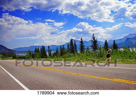 A woman runs along the roadside amidst beautiful scenery View Large Photo Image Picture - A woman runs along the roadside amidst beautiful scenery. Fotosearch