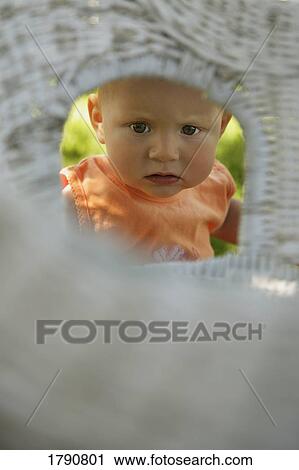 Stock Image - Baby peering through wicker chair. Fotosearch