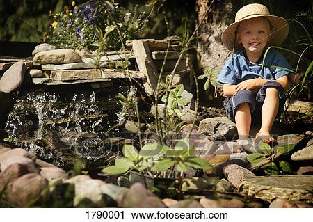 Boy sitting by garden waterfall View Large Photo Image Stock Image - Boy sitting by garden waterfall. Fotosearch