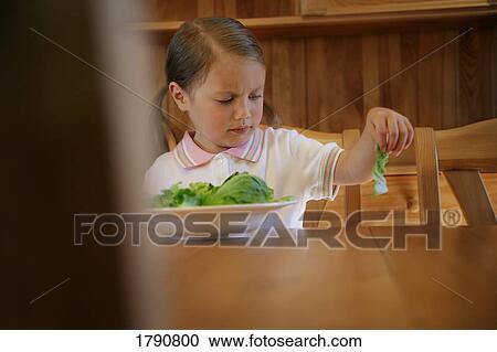Stock Image - Child stares in disgust at piece of lettuce. Fotosearch