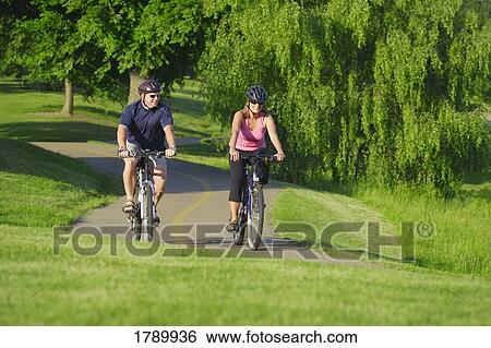 Couple bicycling through park View Large Photo Image Stock Photograph - Couple bicycling through park. Fotosearch