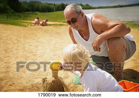 Stock Photo - Grandfather watches over grandchild on beach. Fotosearch