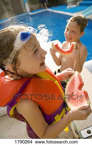 Picture - Kids eating watermelon at poolside. Fotosearch
