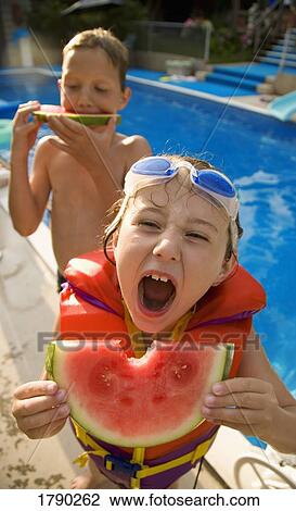 Stock Image - Kids eating watermelon at poolside. Fotosearch