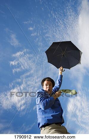 Stock Image - Man holding umbrella floating up into sky. Fotosearch