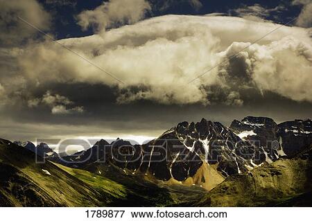 Patches of light find their way through hovering clouds above mountain range View Large Photo Image Stock Photo - Patches of light find their way through hovering clouds above mountain range. Fotosearch