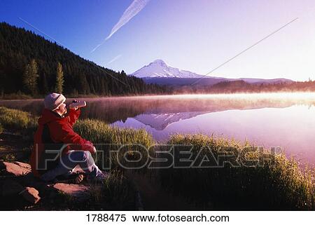 Stock Photography - Person sitting by Mountain Lake shore. Fotosearch