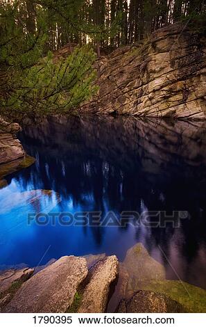 Stock Photography - Rocks and trees reflected in water. Fotosearch