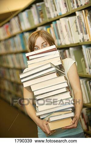Young woman carrying a huge stack of books in a library View Large Photo Image Stock Photo - Young woman carrying a huge stack of books in a library. Fotosearch