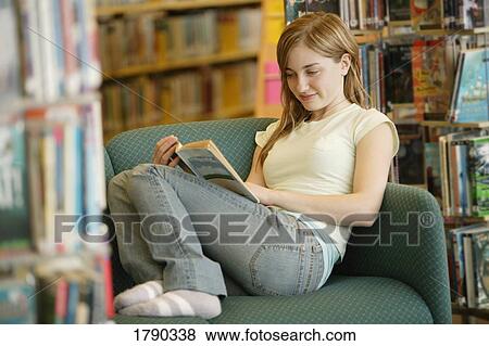 Young woman reading a book in a library View Large Photo Image Stock Photo - Young woman reading a book in a library. Fotosearch