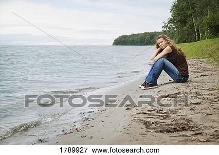 Stock Photo - Young woman sitting on a beach. Fotosearch