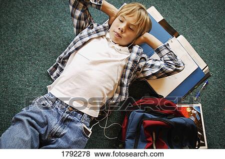 Stock Photo - Boy laying on floor listening to music while doing homework. Fotosearch