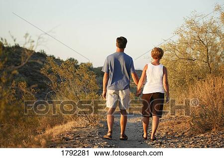 Couple walking down path hand-in-hand View Large Photo Image Stock Image - Couple walking down path hand-in-hand. Fotosearch