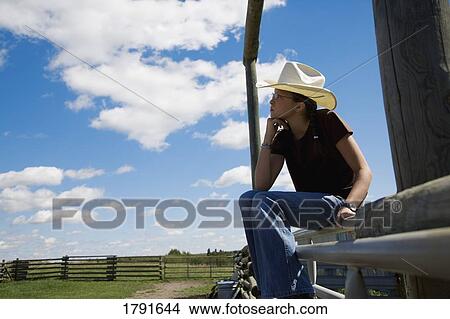 Picture - Cowgirl sitting on gate. Fotosearch