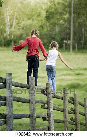 Stock Image - Girls walking on corral fence. Fotosearch