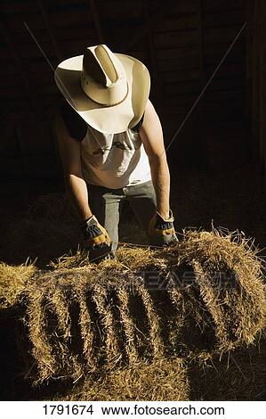 Man in cowboy hat moves hay bale View Large Photo Image Picture - Man in cowboy hat moves hay bale. Fotosearch