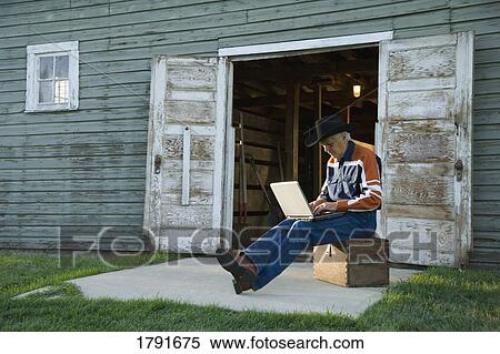 Man in cowboy hat working on computer outside of barn View Large Photo Image Stock Photography - Man in cowboy hat working on computer outside of barn. Fotosearch