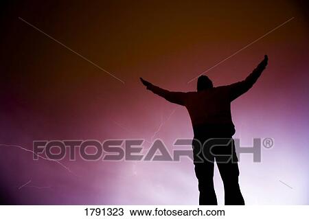 Stock Image - Man with outstretched arms in lightning storm. Fotosearch