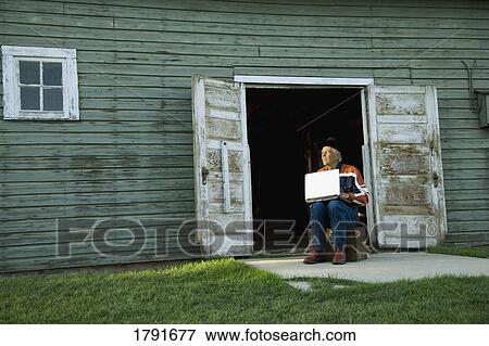 Stock Photo - Man working on computer outside of barn or shed. Fotosearch