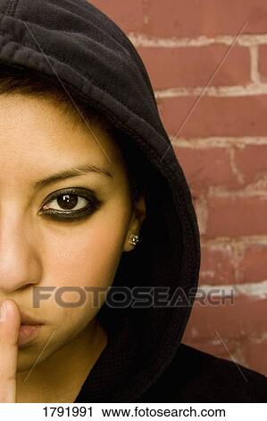 Stock Image - Woman in black hood making quiet sign with finger on lips. Fotosearch