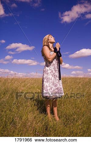 Stock Photograph - Woman praying in a field. Fotosearch