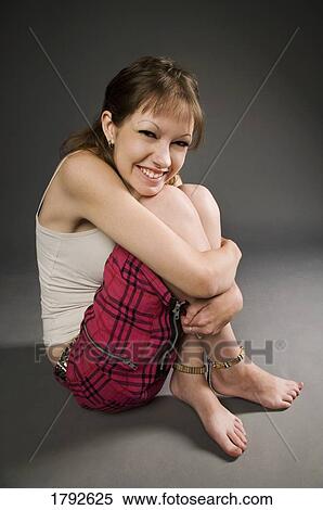 Stock Photography - Woman sitting down hugging knees and smiling. Fotosearch